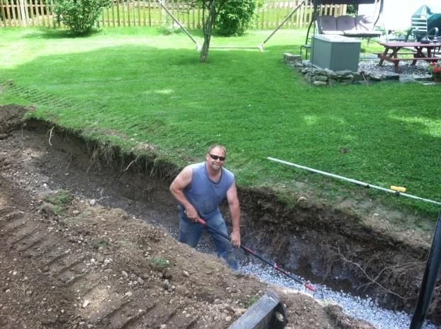 Man in blue shirt standing in a ditch during backyard construction or landscaping work
